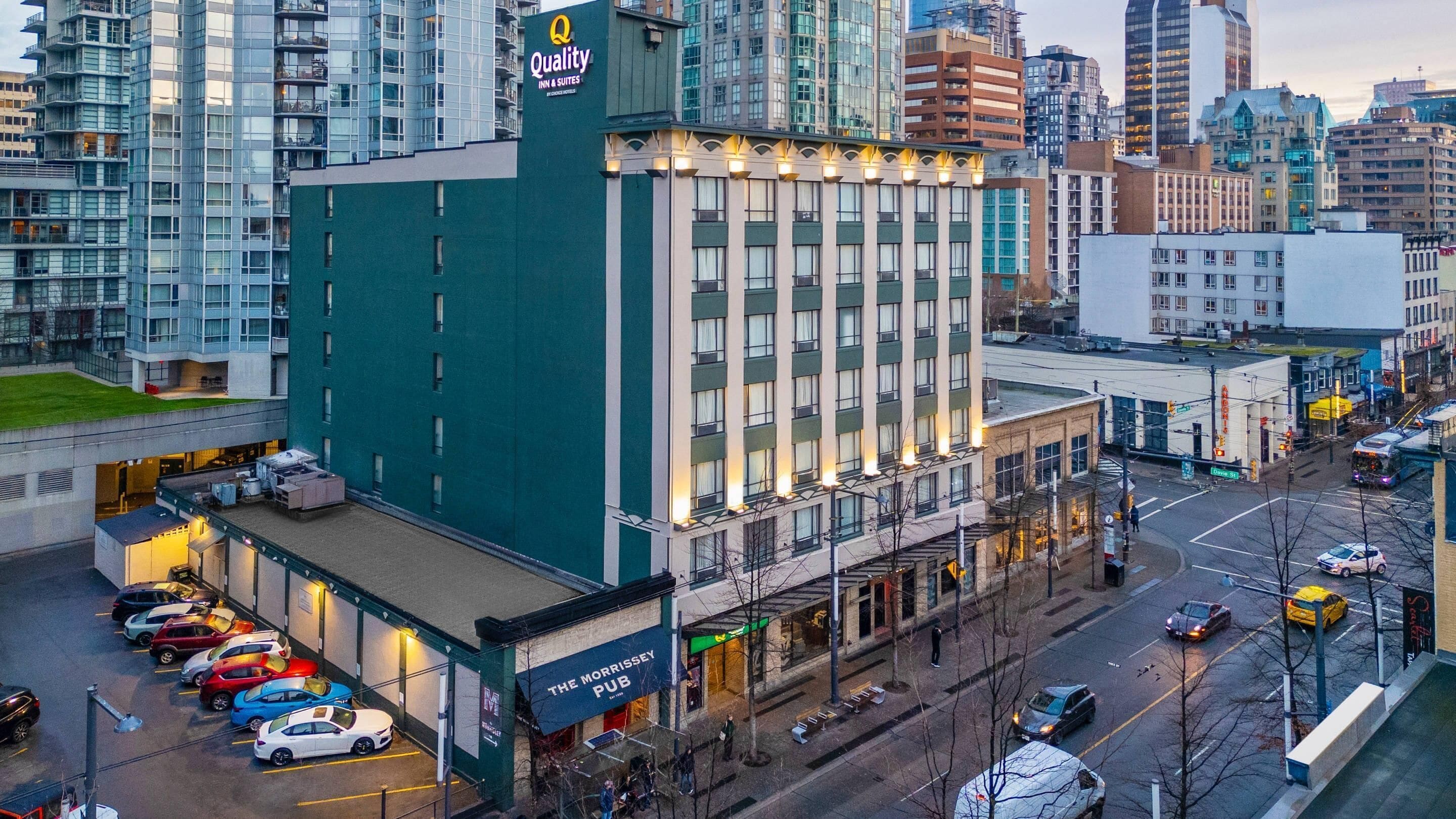 A hotel with a green facade, multiple floors, and a parking lot with cars.