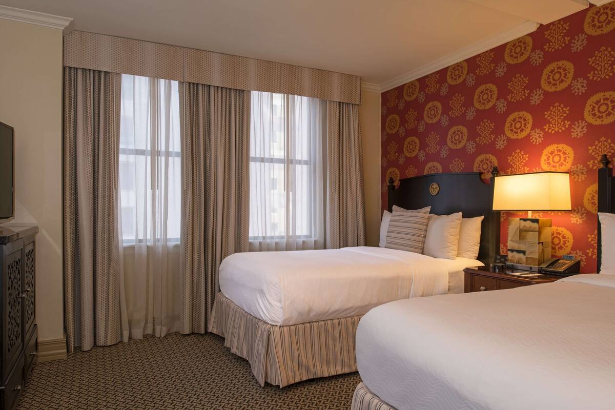 Habitación de hotel con dos camas, televisión, escritorio y pared con diseño.