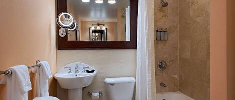 Une salle de bain équipée d’un lavabo, de toilettes et d’une baignoire. Un miroir est placé au-dessus du lavabo, et un porte-serviettes contient des serviettes.