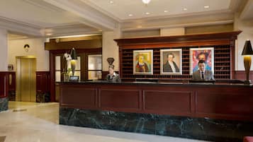 Zona de recepción de un hotel con mostrador de mármol, obras de arte enmarcadas y un mostrador de recepción.