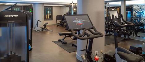 Un gimnasio con diversos equipos de ejercicio, incluyendo cintas de correr, una máquina de press de banca y una bicicleta estática.