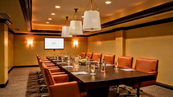 A conference room with a long table, orange chairs, and a projector screen.