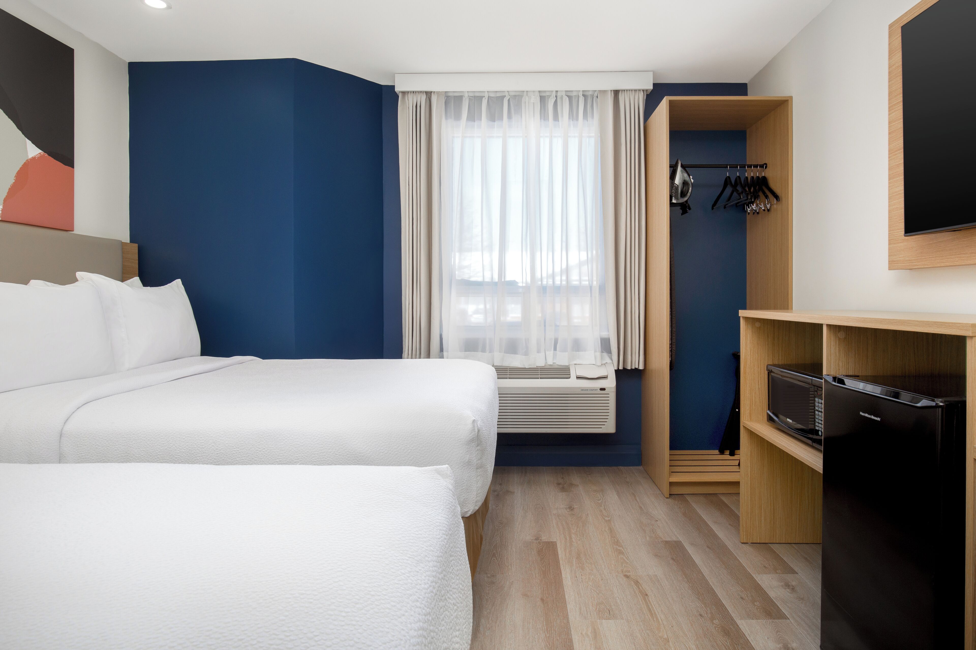 Quarto de hotel com duas camas, um guarda-roupa, uma televisão e uma janela com cortinas.