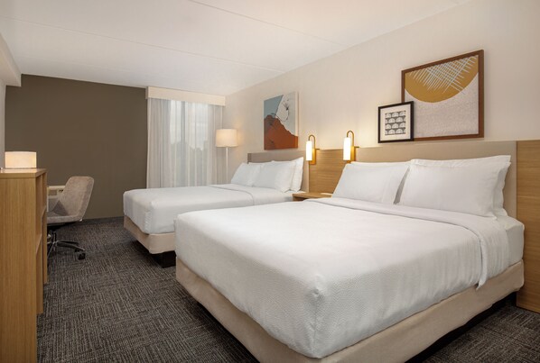 Una habitación de hotel con dos camas, un escritorio, una silla y una lámpara.