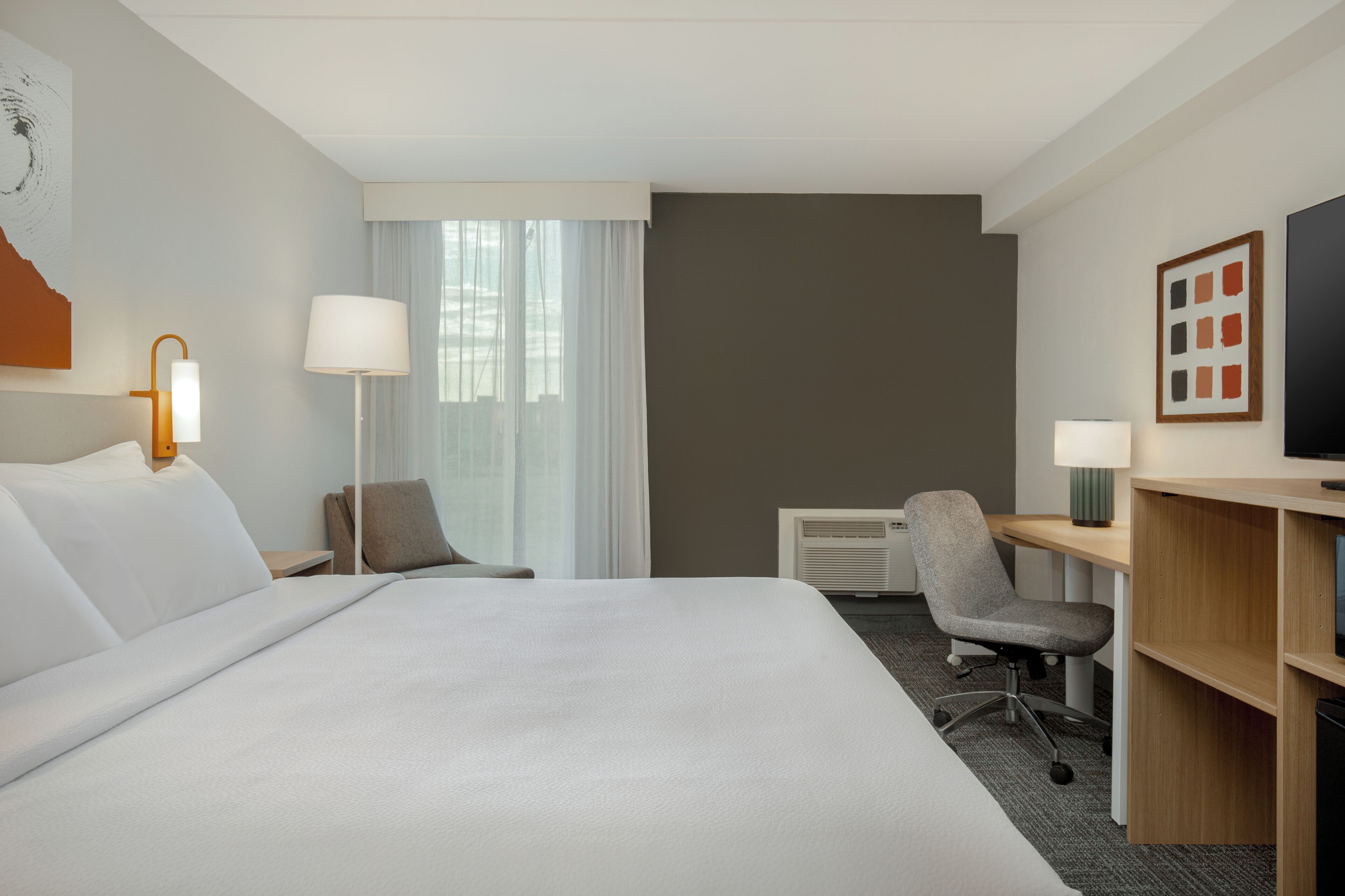 Une chambre d’hôtel avec un grand lit, un bureau avec une chaise, une télévision et une fenêtre avec des rideaux.