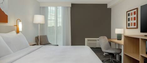 Una camera d'albergo con un letto grande, una scrivania con una sedia, una televisione e una finestra con tende.