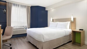 Ein Hotelzimmer mit Bett, Schreibtisch, Stuhl und einem fensterbepflanzten Fenster.
