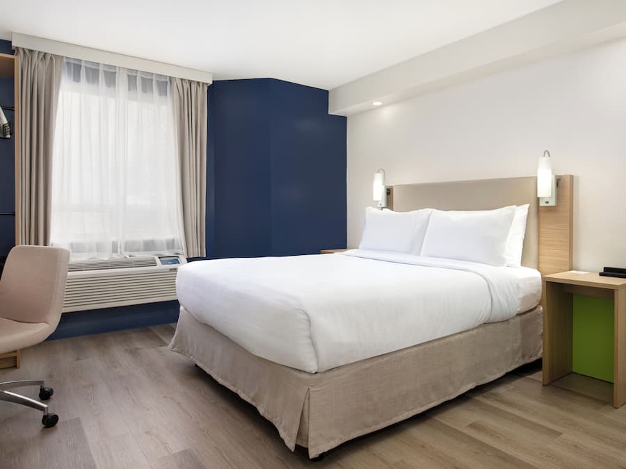 Una habitación de hotel con cama, escritorio, silla y ventana con cortinas.