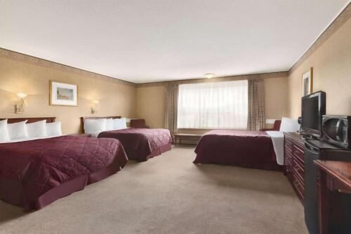 A hotel room with two beds, a television, a dresser, and a window with curtains.
