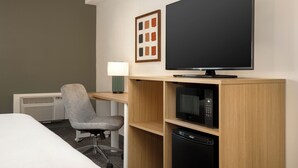 Ein Hotelzimmer mit Bett, Schreibtisch mit Lampe, Fernseher, Mikrowelle und Geschirrspüler.