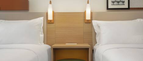 A hotel room with two beds, a wooden headboard, bedside lamps, a green ottoman, and a framed artwork on the wall.