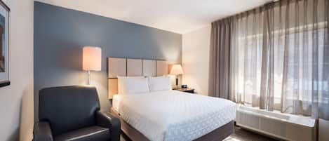 Habitación de hotel con cama, una silla, dos lámparas de noche, ventana con cortinas y un calentador fijado a la pared.