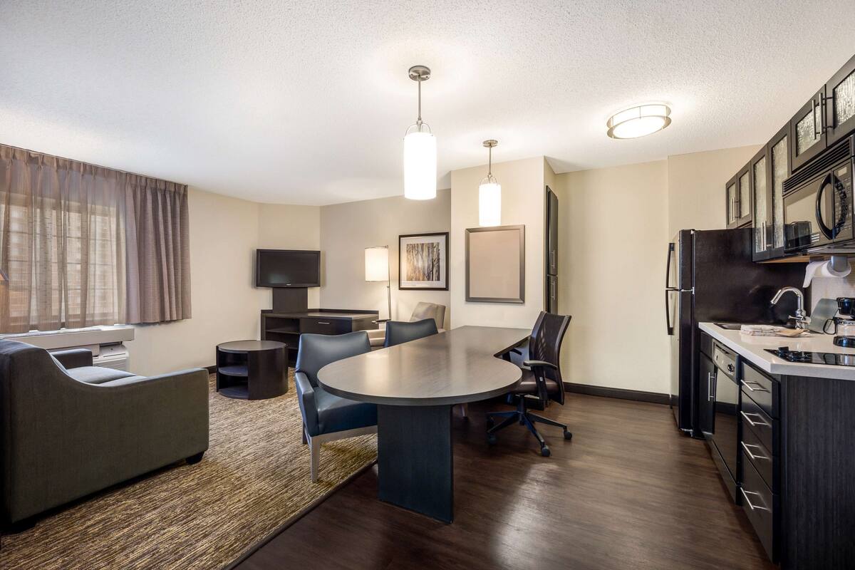 A modern, well-lit living room with a dining area, kitchen, and a flat-screen TV.