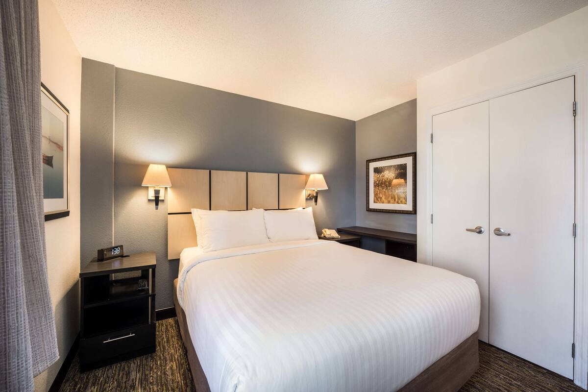 A hotel room with a large bed, bedside lamps, a nightstand, a wardrobe, and a framed picture on the wall.