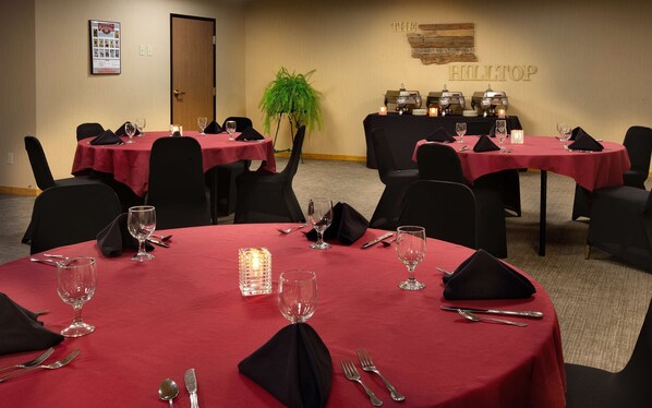A conference room with round tables, black chairs, and red tablecloths.