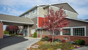 A multi-story building with a brick facade, a covered entrance, and a landscaped garden with various plants and flowers.