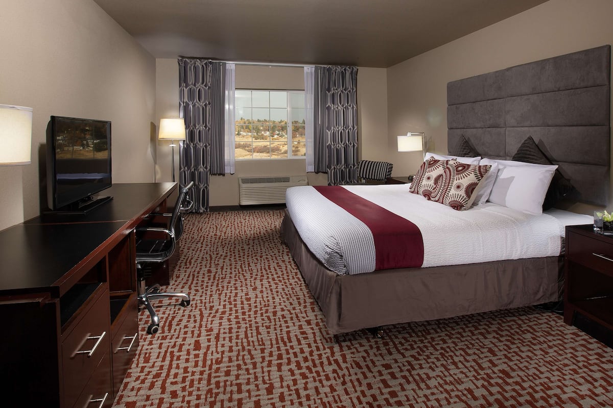 A hotel room with a large bed, a desk with a television, a chair, and a window with curtains.