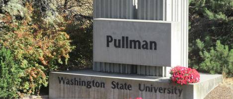 A stone monument with the inscription "Pullman Washington State University" surrounded by greenery.