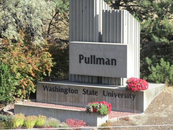 A stone monument with the inscription "Pullman Washington State University" surrounded by greenery. - Coast Hilltop Inn (Pullman)