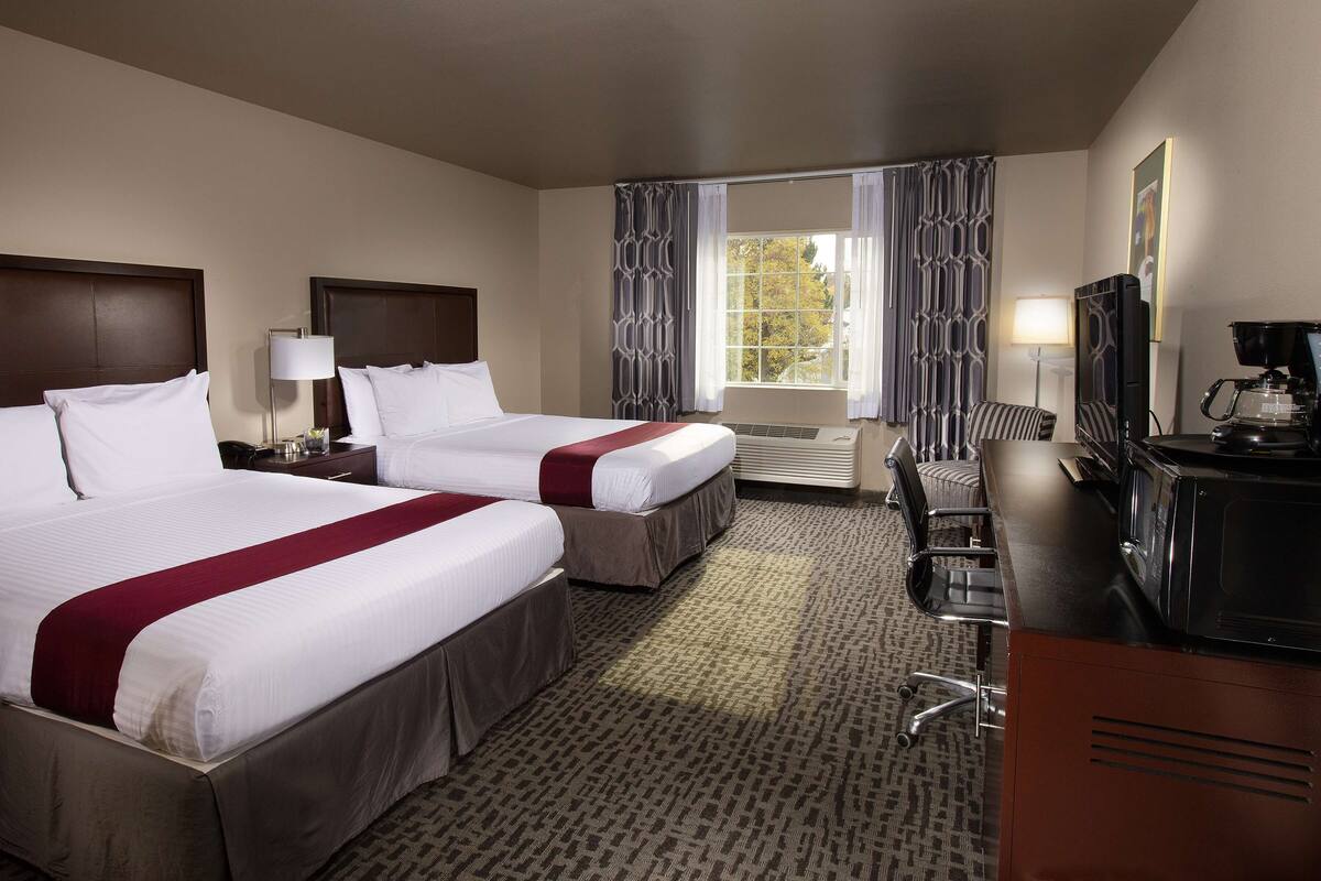 A hotel room with two beds, a desk with a coffee maker, a TV, and a window with curtains.