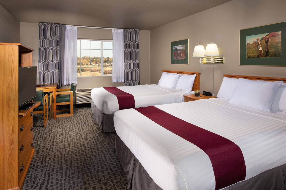 A hotel room with two beds, a desk, a chair, a TV, and a window with curtains.