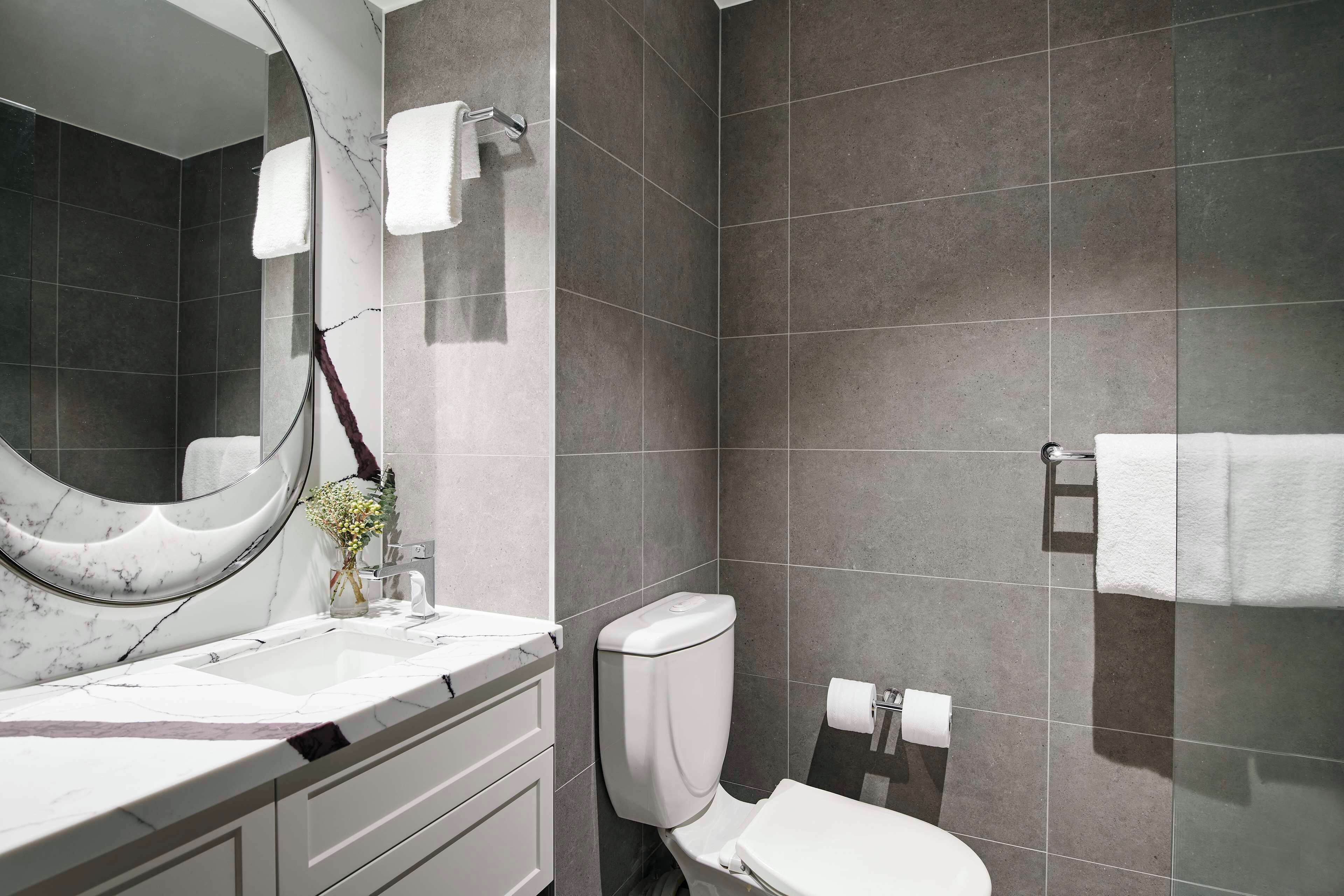 A modern bathroom with a marble sink, a toilet, and a large mirror.