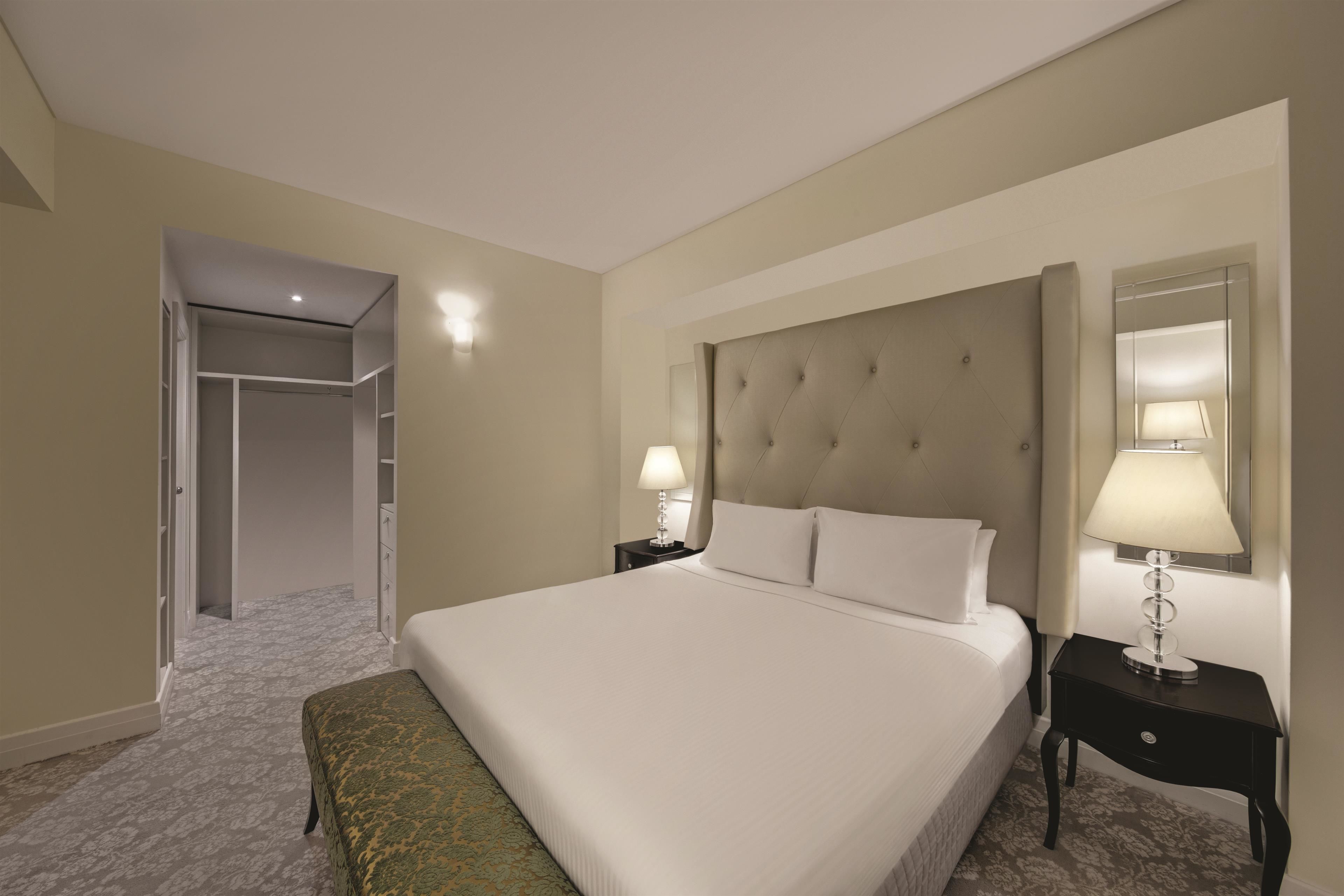 A hotel room with a large bed, two bedside tables with lamps, a wardrobe, and a mirror on the wall.