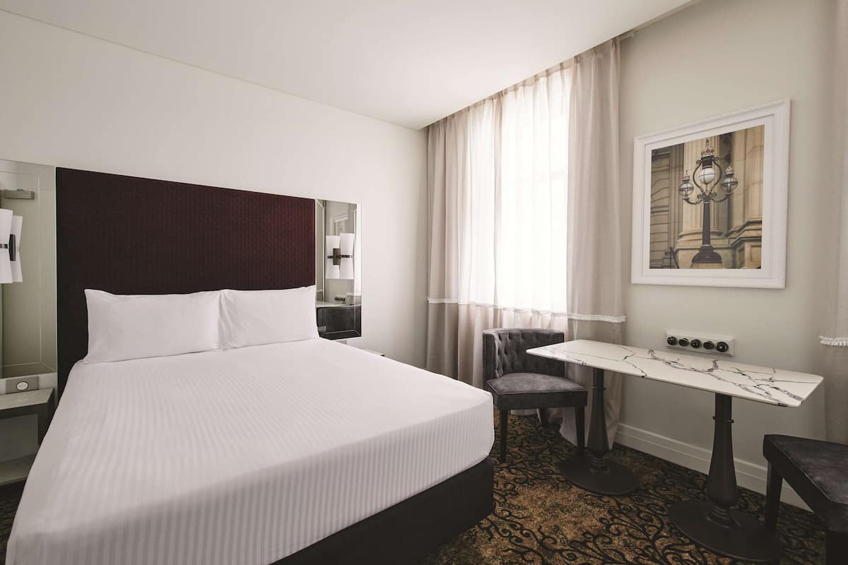 A hotel room with a large bed, a small table, a chair, and a desk.