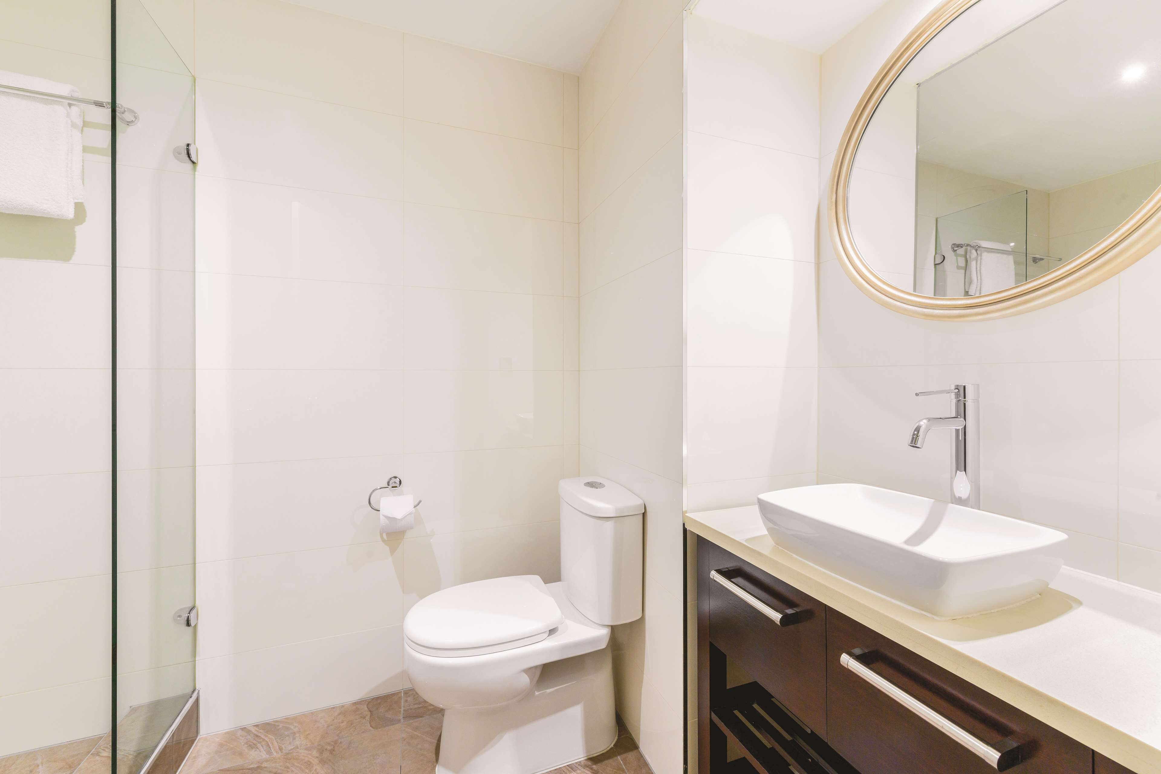 A modern bathroom with a glass shower enclosure, a white toilet, and a vanity with a large mirror and a vessel sink.