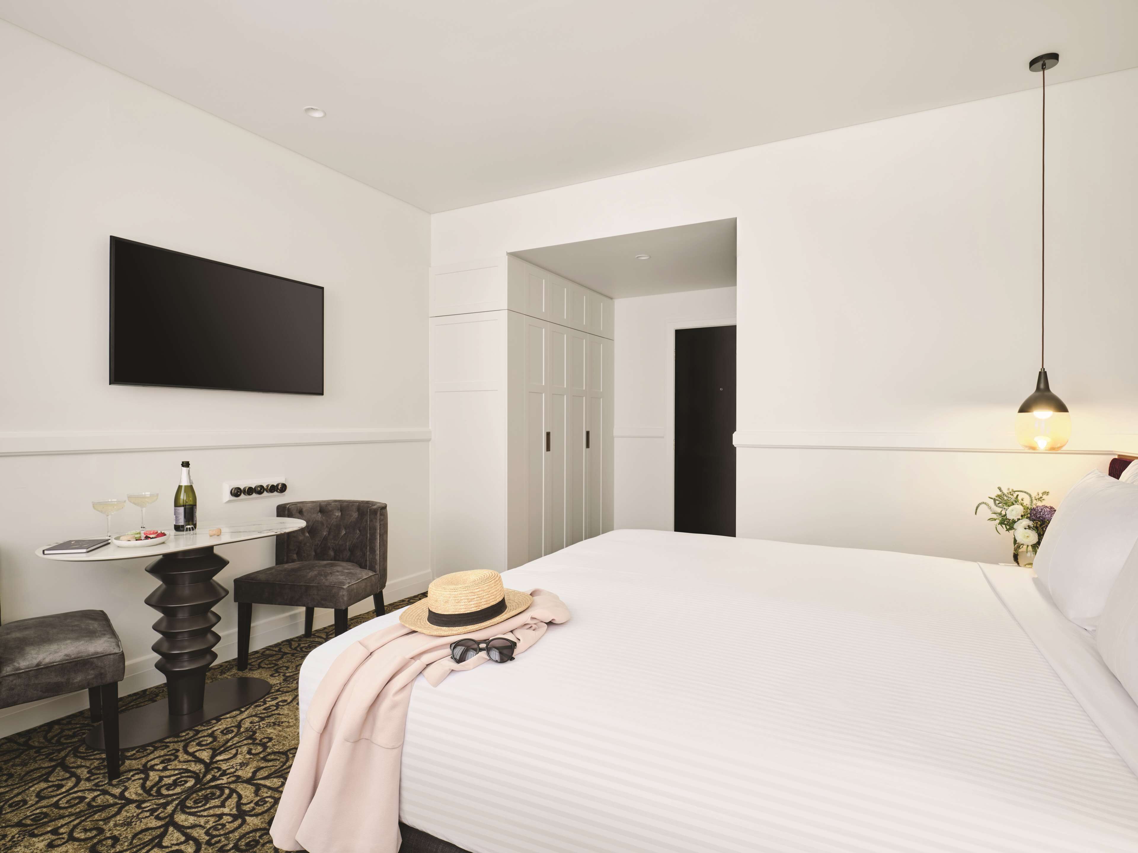 A hotel room with a bed, a desk with a chair, a television, and a wardrobe.