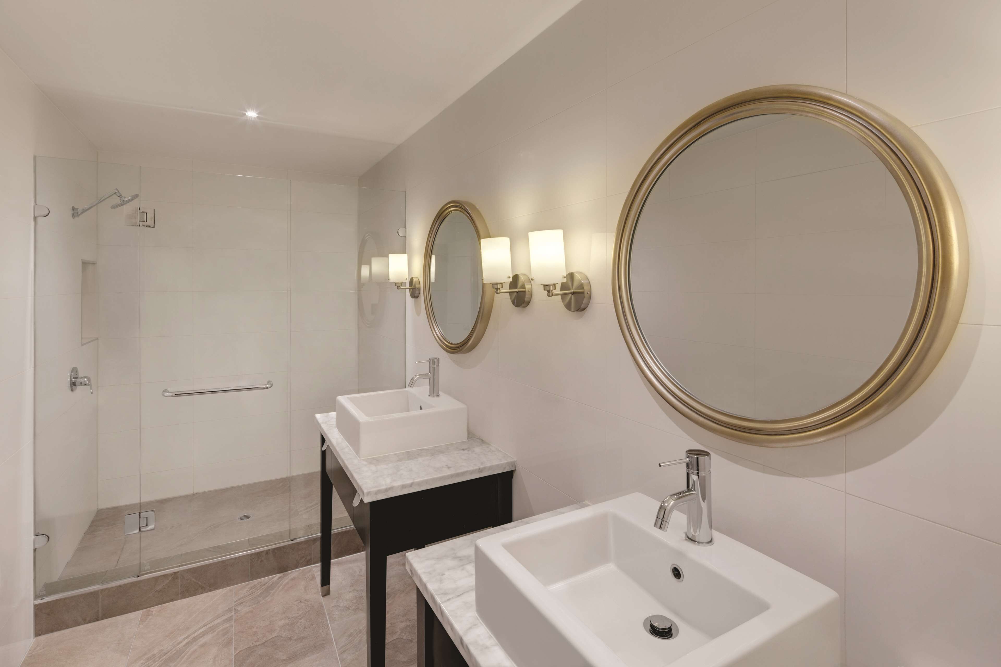 A modern bathroom with two sinks, a shower, and large mirrors.