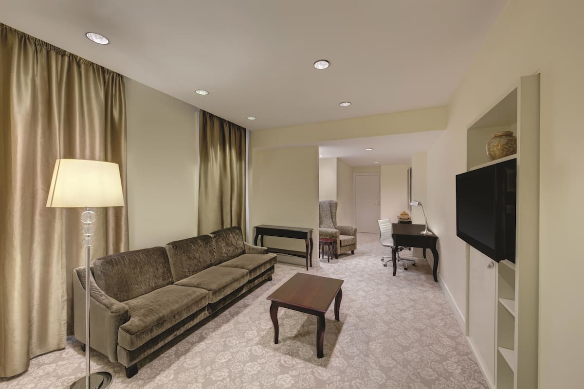 A hotel room with a sofa, a coffee table, a TV, a desk, and a lamp.