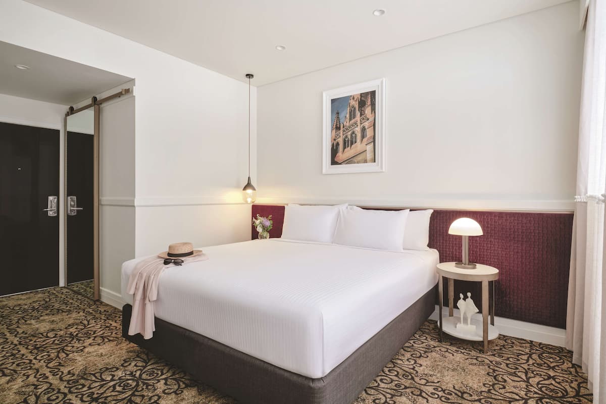 A hotel room with a large bed, a bedside table with a lamp, a framed picture on the wall, and a patterned carpet.