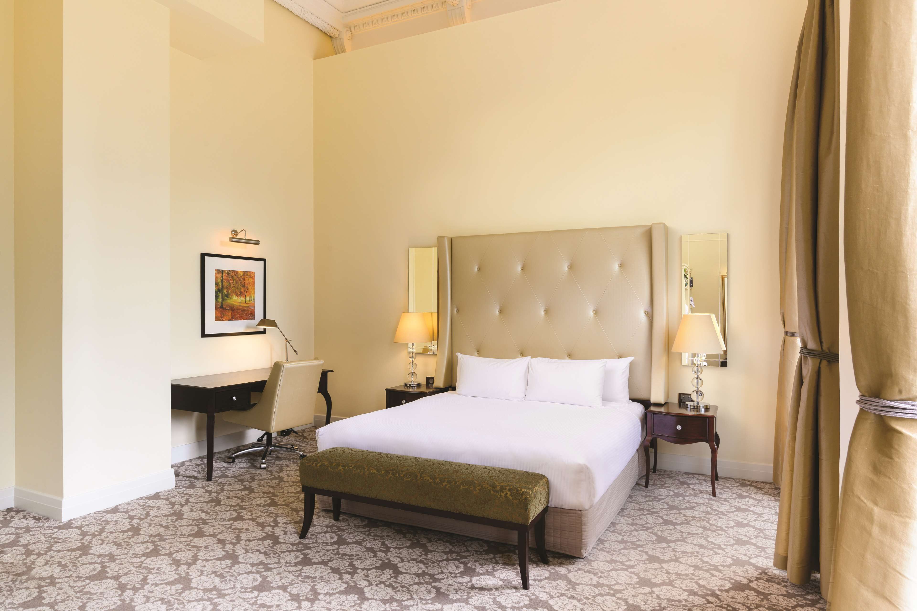 A hotel room with a large bed, bedside tables with lamps, a desk, and a framed picture on the wall.