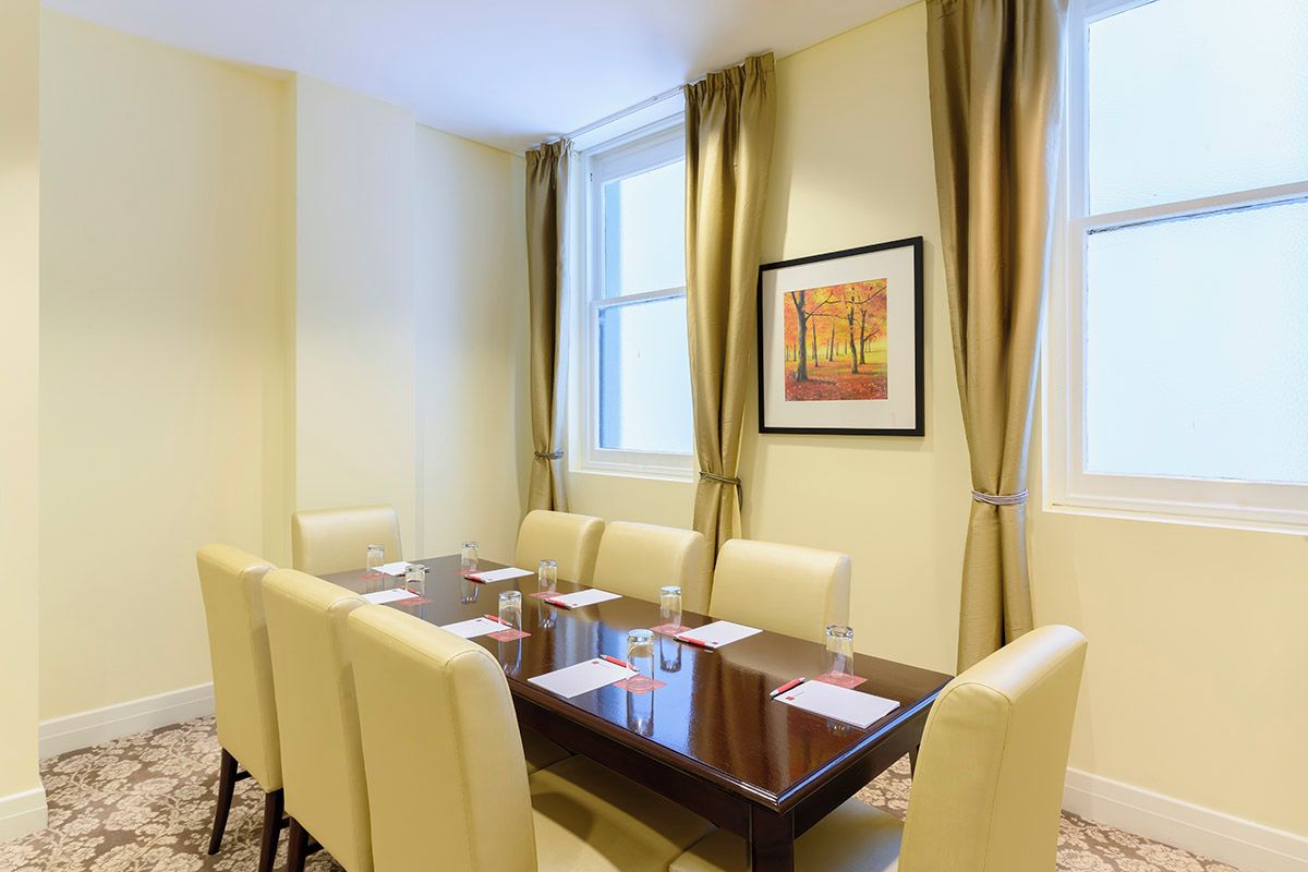 A conference room with a wooden table, six chairs, and a framed painting on the wall.