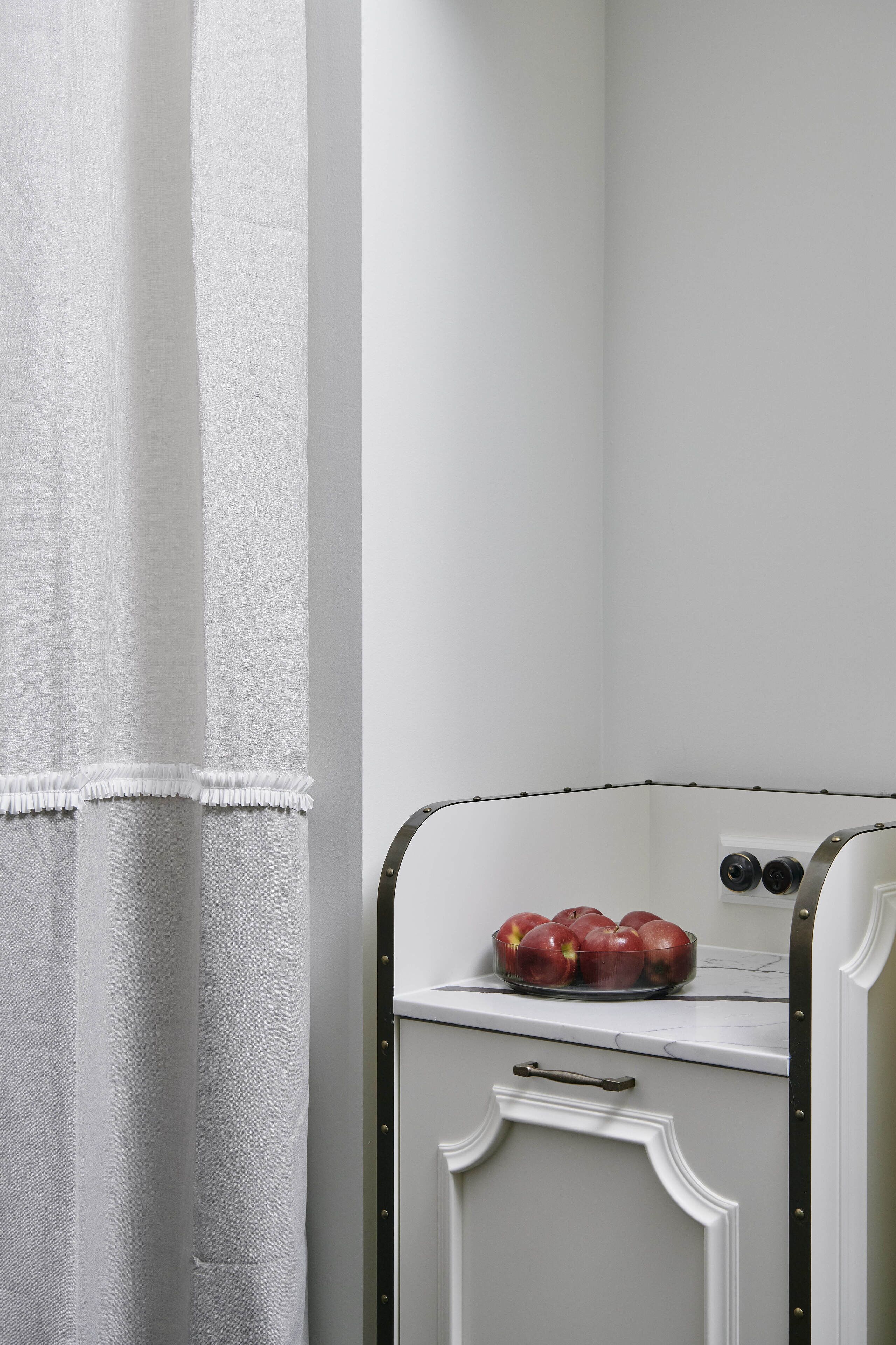 A kitchen with a white cabinet, a white countertop, and a bowl of apples.