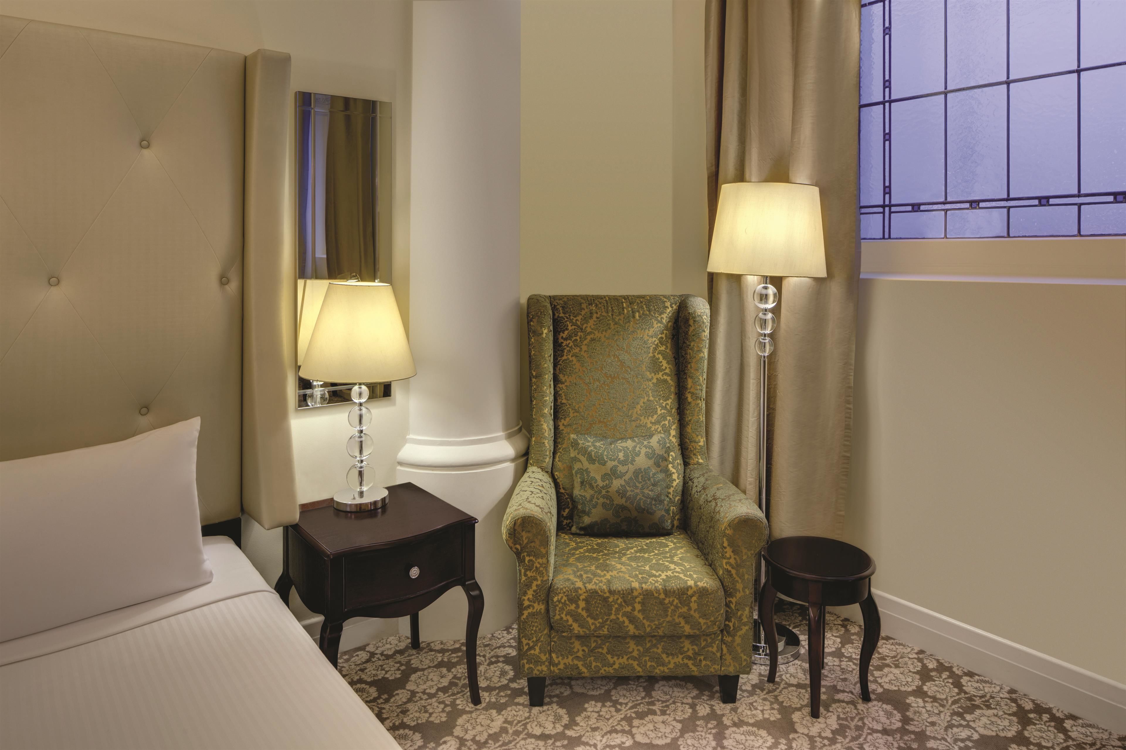A hotel room with a bed, two bedside tables with lamps, a chair, and a window with curtains.