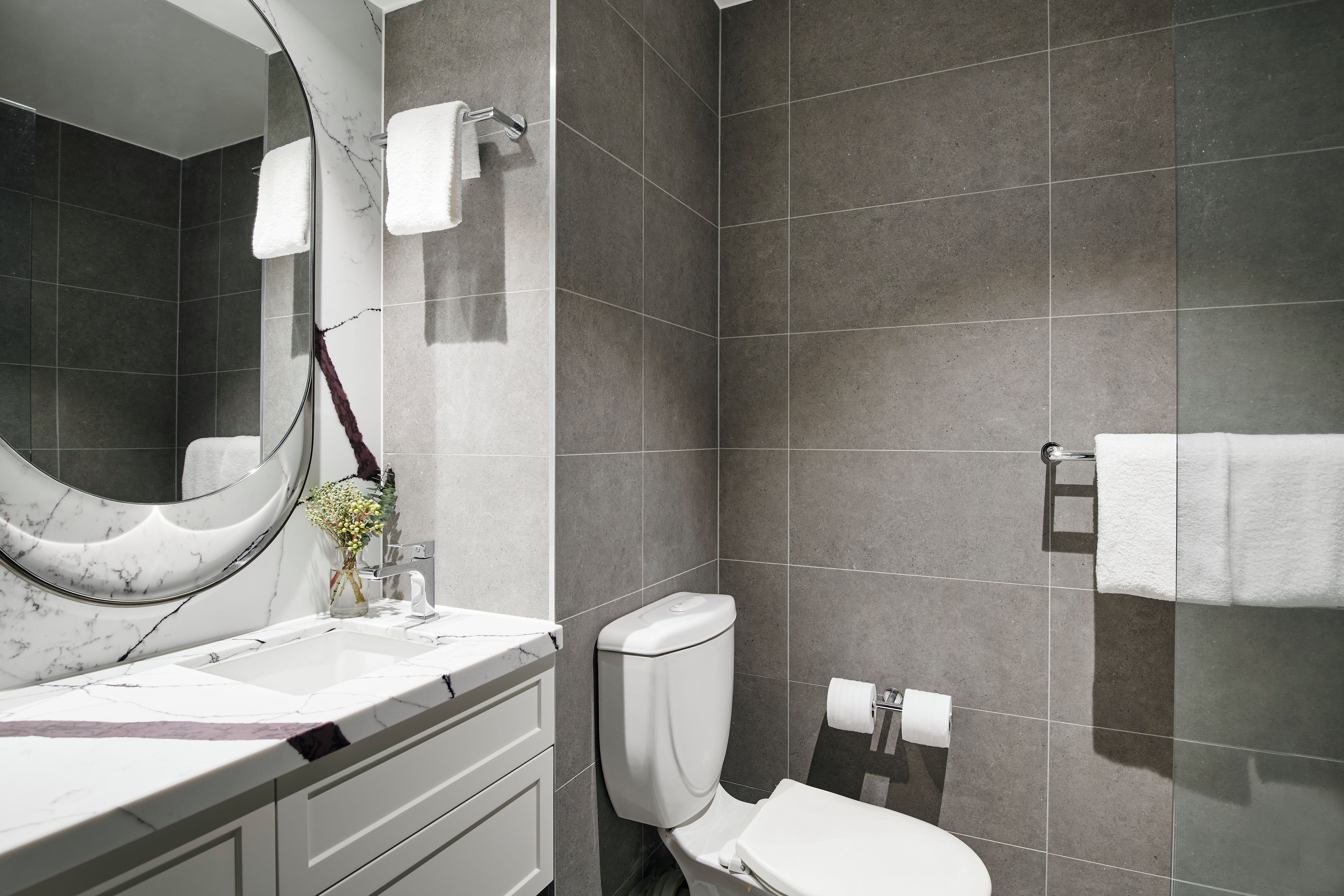 Een moderne badkamer met een marmeren wastafel, toilet en douchehoek.