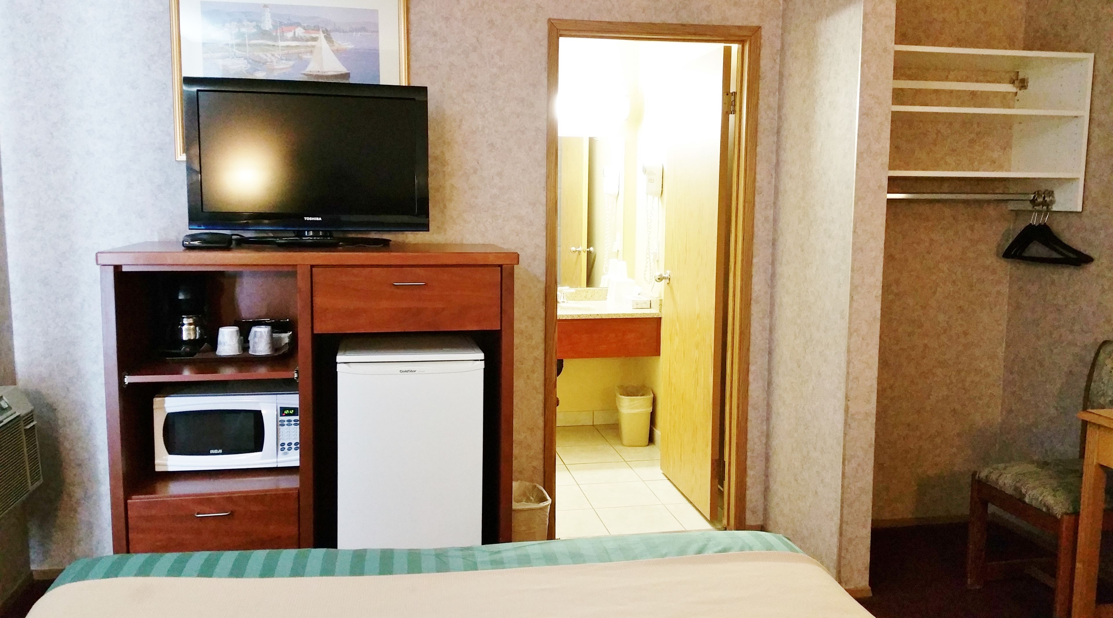 A hotel room with a bed, a TV on a wooden cabinet, a microwave, and a refrigerator.