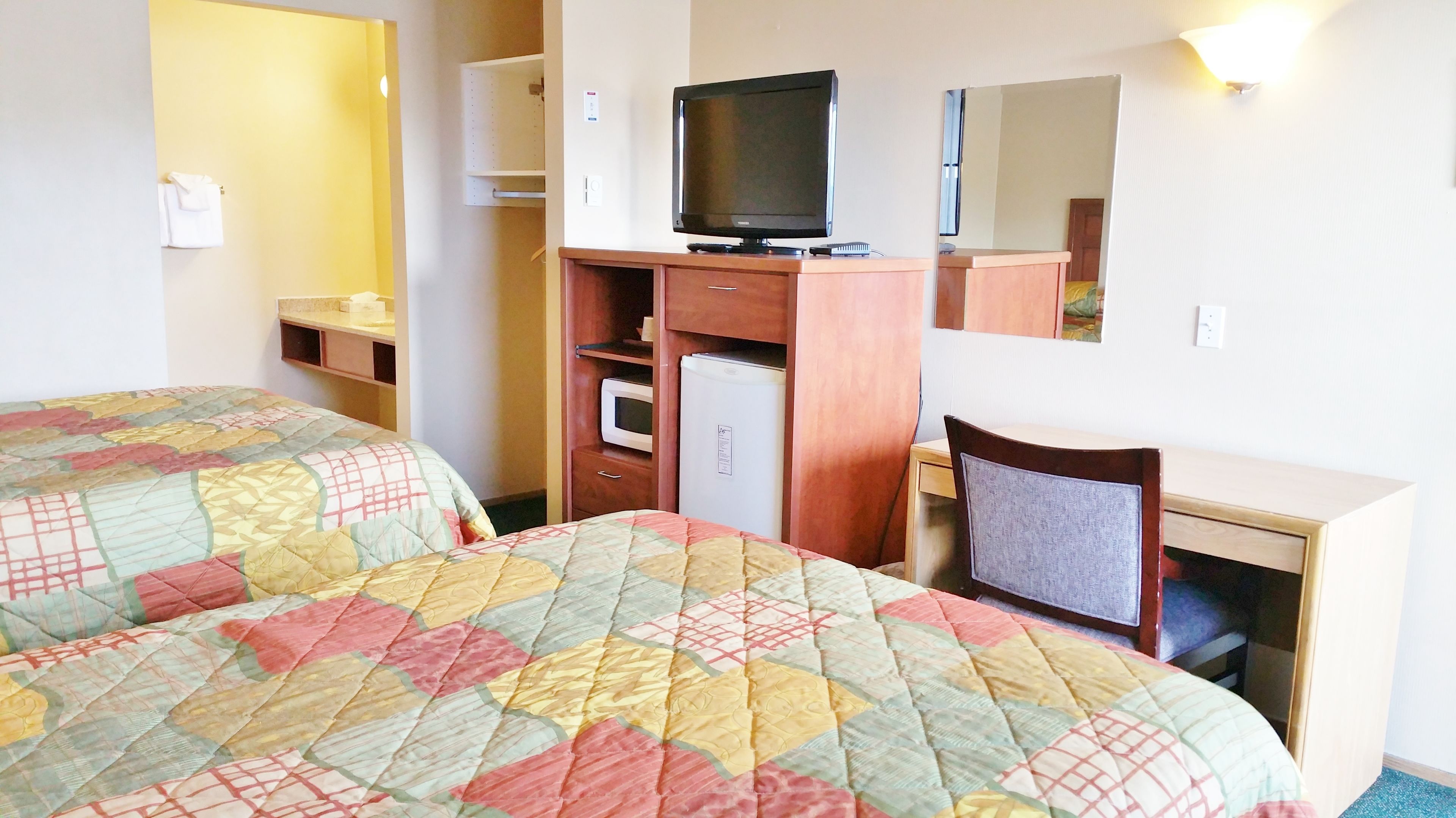 Une chambre d’hôtel avec deux lits, un bureau, une télévision, un réfrigérateur et un miroir.