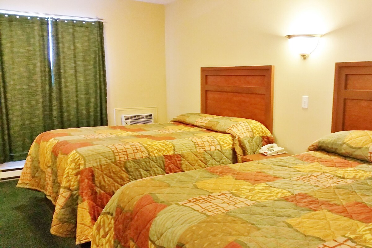 A hotel room with two beds, a telephone, and a wall-mounted light fixture.
