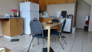 A compact kitchen with a refrigerator, a sink, and a dining area with two chairs and a table.