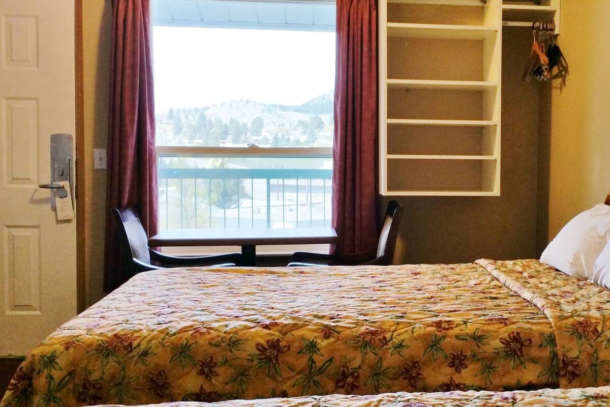Une chambre d’hôtel comprenant un lit, une table de chevet avec un téléphone, une fenêtre avec des rideaux, une chaise et un placard intégré.