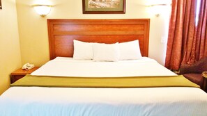 A hotel room with a large bed, a wooden headboard, white bedding, a bedside telephone, and a framed picture on the wall. - Alpine Motel (Kamloops)