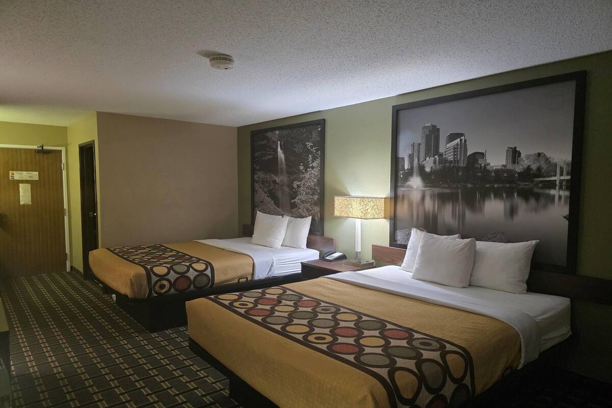 A hotel room with two beds, a cityscape view, a patterned bedspread, and a lamp.