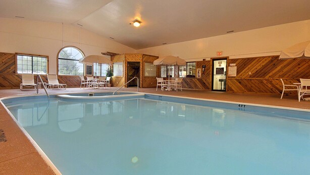 An indoor swimming pool with lounge chairs and umbrellas, wooden panel walls, and large windows. - Super 8 by Wyndham Coshocton Roscoe Village (Coshocton)