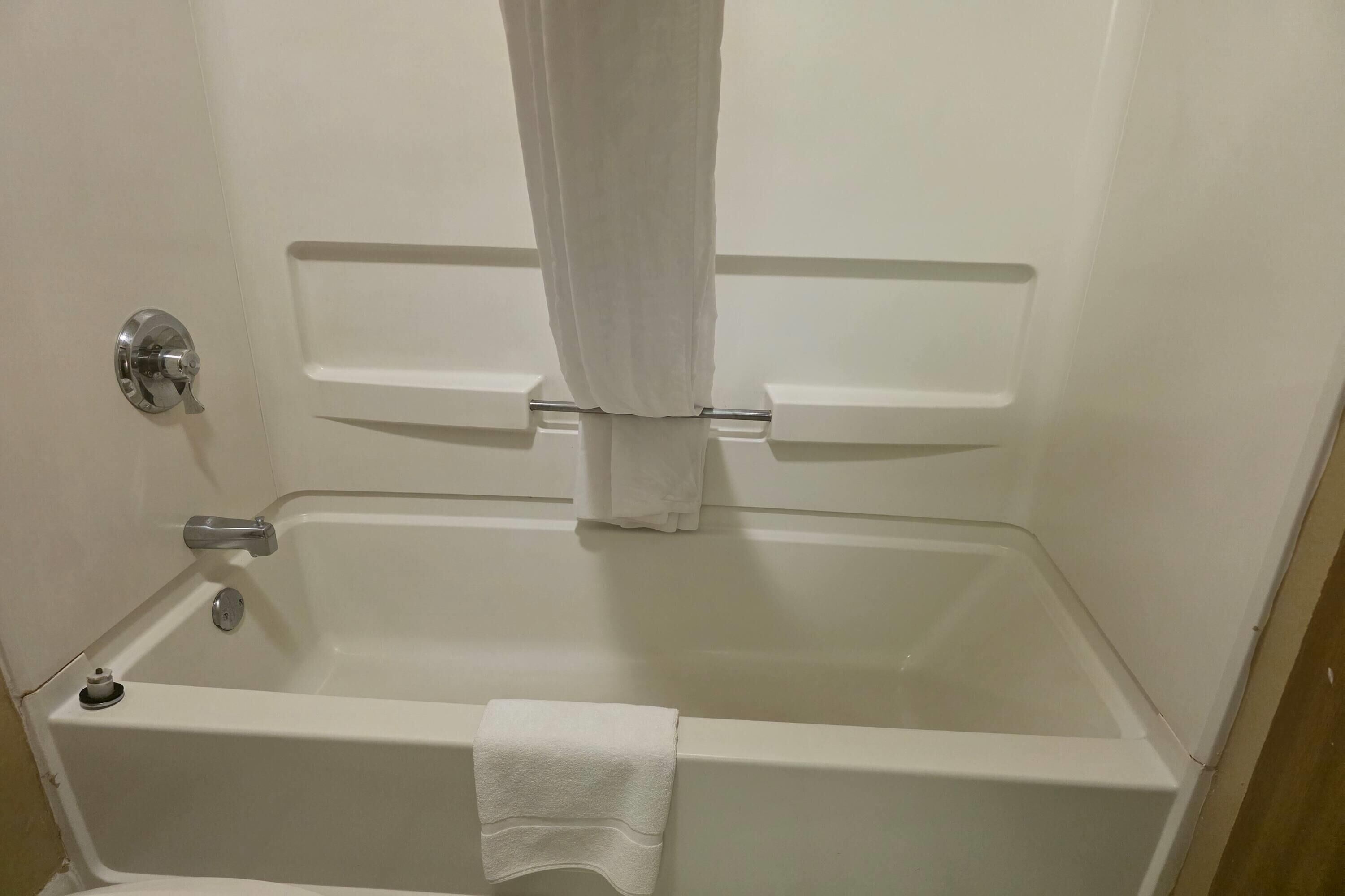 A white bathtub with a shower curtain, a towel, and a faucet.