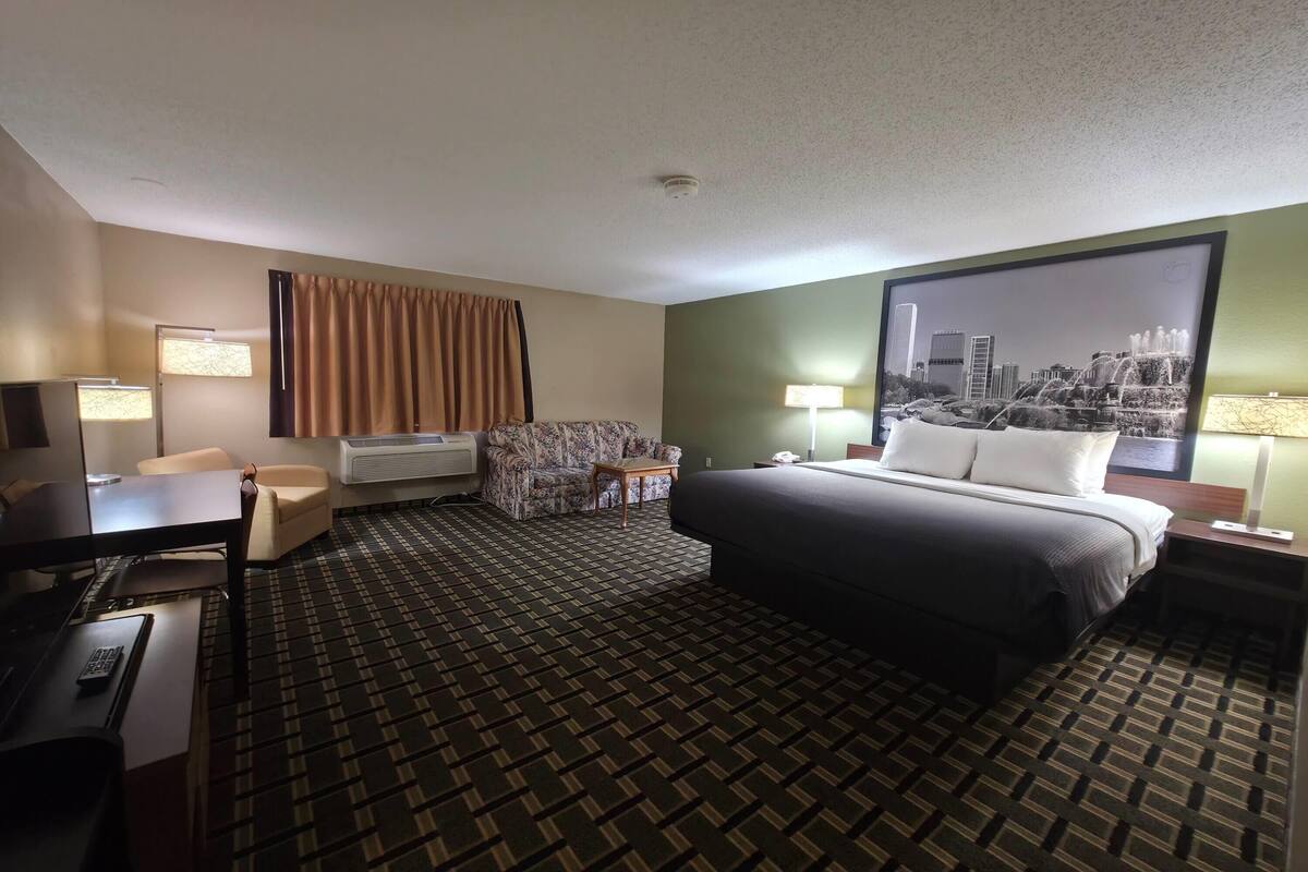 A hotel room with a bed, a desk, a chair, an air conditioner, a lamp, and a cityscape view.