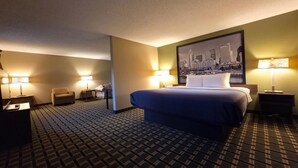 A hotel room with a bed, two bedside tables, a chair, a desk, and a cityscape painting on the wall. - Super 8 by Wyndham Coshocton Roscoe Village (Coshocton)