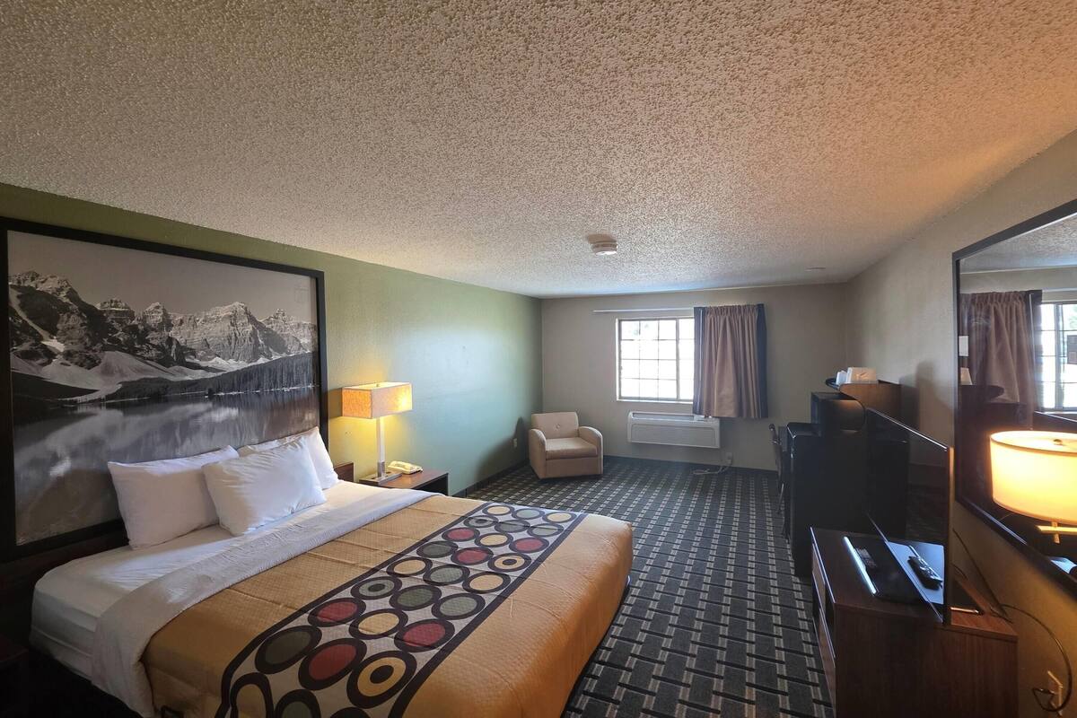 A hotel room with a bed, a desk, a chair, a television, and a window with curtains.